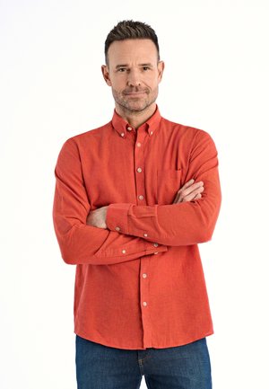 Camicia rossa a maniche lunghe con bottoni, dotata di tasca, in tessuto testurizzato e con bottoni bianchi in contrasto, abbinata a jeans blu di denim.