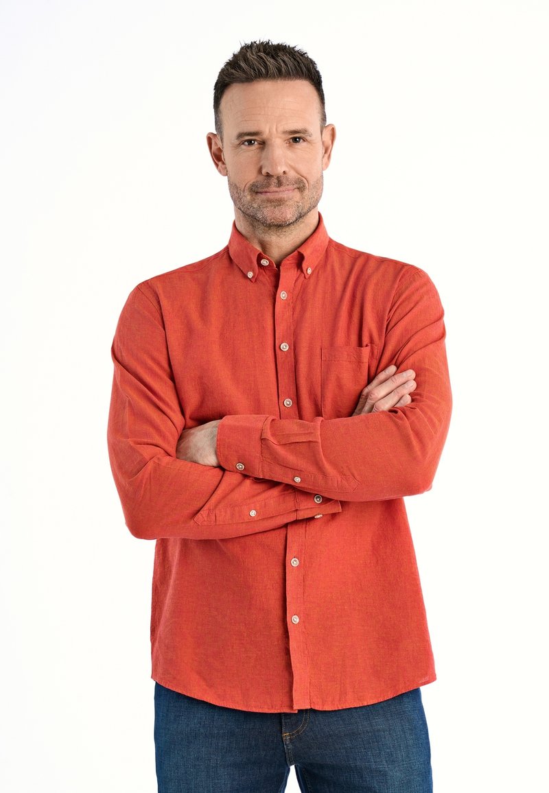 Czerwona, długosleeva koszula zapinana na guziki z kieszonką, teksturowana tkanina i kontrastowe białe guziki, w połączeniu z niebieskimi dżinsami.