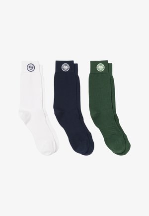 Tre paia di calzini a metà polpaccio in bianco, blu navy e verde scuro con una toppa rotonda con il logo Roland Garros vicino alla parte superiore su sfondo bianco.