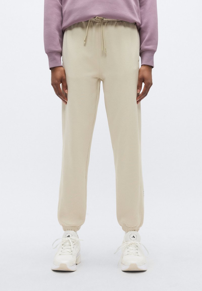 Μπεζ παντελόνι jogging από απαλό υλικό, με λάστιχο στη μέση, ελαστικές μανσέτες και πλαϊνές τσέπες, συνδυασμένο με λευκά αθλητικά παπούτσια.