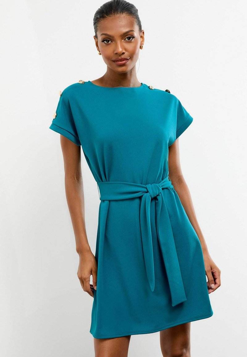 Rochie turcoaz cu mâneci scurte, un centură la talie și butoane decorative la umeri. Material neted cu un design fluid.