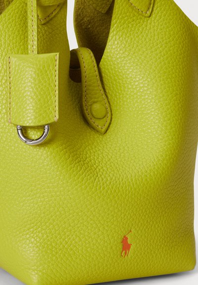 Mala torba od teksturirane kože u jarko limunasto zelene boje, s zaobljenim oblikom, srebrnim metalnim prstenom i izbočenim logotipom.