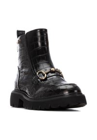 Botín negro hecho de cuero con estampado de cocodrilo, con suela gruesa, detalles de cadena de metal y una lengüeta en la parte trasera.