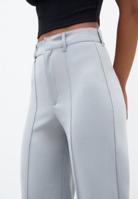 Gros plan d'une personne portant un pantalon taille haute gris clair ajusté avec des coutures apparentes et un top noir court.