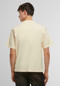 Lyhythihainen, vaalea beige T-paita, joka on valmistettu pehmeästä puuvillasta. Paitassa on klassinen pyöreä kaula-aukko ja normaali istuvuus. Ei näkyviä logoja tai kuvioita.