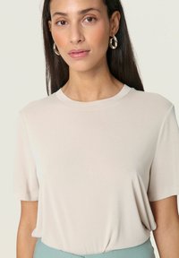Beige kortærmet t-shirt lavet af glat stof, med rund halsudskæring og let drapering, kombineret med lyseblå underdele.