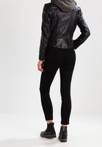 Zwarte leren jas met een gestructureerde afwerking, grijze hoodie eronder, zwarte skinny jeans en zwarte enkellaarsjes met ritsen.