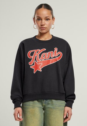 Svart crewneck genser med en rød grafisk trykk som har ordet "Kani" og en stjerne. Stoffet ser mykt ut med en avslappet passform.