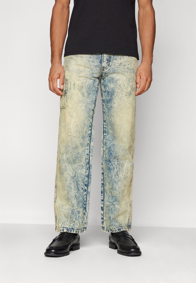 Lyseblå, slitte vide jeans med en falmet finish, med en sidelomme i cargo-stil og synlige sømdetaljer. Svarte sko nedenfor.