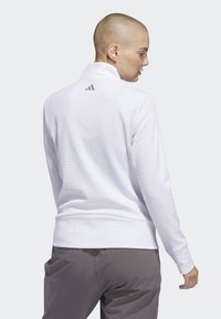 Pulôver branco de mangas longas com gola alta, tecido texturizado e logótipo cinza da Adidas nas costas. Combinado com calças cinza claro.