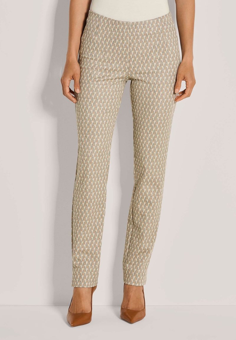 Aangesloten beige broek met een geometrisch patroon in lichte kleuren. Glad stof, middelhoge taille en taps toelopende pijpen, gecombineerd met bruine hakken.