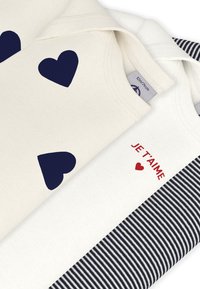 Τρία μπλουζάκια: ένα κρεμ με μπλε ναυτικά καρδιές, ένα λευκό με κόκκινο κείμενο "JE T'AIME" και καρδιά, και ένα με ρίγες σε μπλε ναυτικό και λευκό.