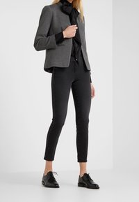 Veste classique grise avec un nœud papillon en satin noir, pantalon noir ajusté et chaussures en cuir noires à lacets. Tissu lisse et design ajusté.