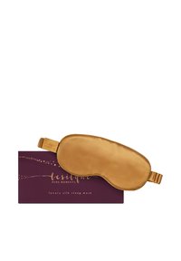 Goldene Schlafmaske aus Seide mit elastischem Band, liegend auf einer dunkelvioletten Schachtel mit der Aufschrift "Lesilque Pure Moments luxury silk sleep mask."