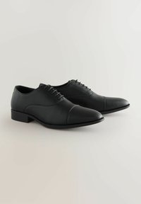 Zapatos de vestir de cuero negro con un acabado texturizado, diseño de punta cerrada y suela de goma plana, con cierre de cordones y cuello acolchado.