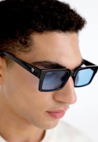 Ochelari de soare negri, rectangulari, cu lentile de un albastru nuanțat, care prezintă un logo pe lateral și un design elegant, unghiular.