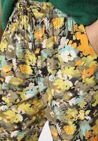 Spodnie w kwiatowy wzór w kolorach żółtym, morskim i czarnym, z talią ze sznurkiem i lekką tkaniną o fakturowanym wykończeniu.