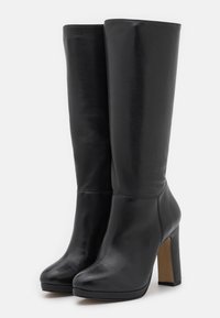Bottes hautes en cuir noir jusqu'aux genoux avec une texture lisse, une forme effilée et un talon haut épais. Elles présentent un bout arrondi et des détails de coutures.
