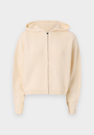 Krátka krémová mikina na zips s uvoľneným strihom, rebrovanými manžetami a lemom, vybavená kapucňou so šnúrkou a textúrovaným pleteným materiálom.