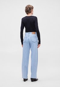 Ανοιχτό μπλε παντελόνι με φαρδιά πόδια και ψηλή μέση, με πίσω τσέπες και καφέ δερμάτινη λογότυπο στο πίσω μέρος. Μαύρη μπλούζα με μακριά μανίκια.