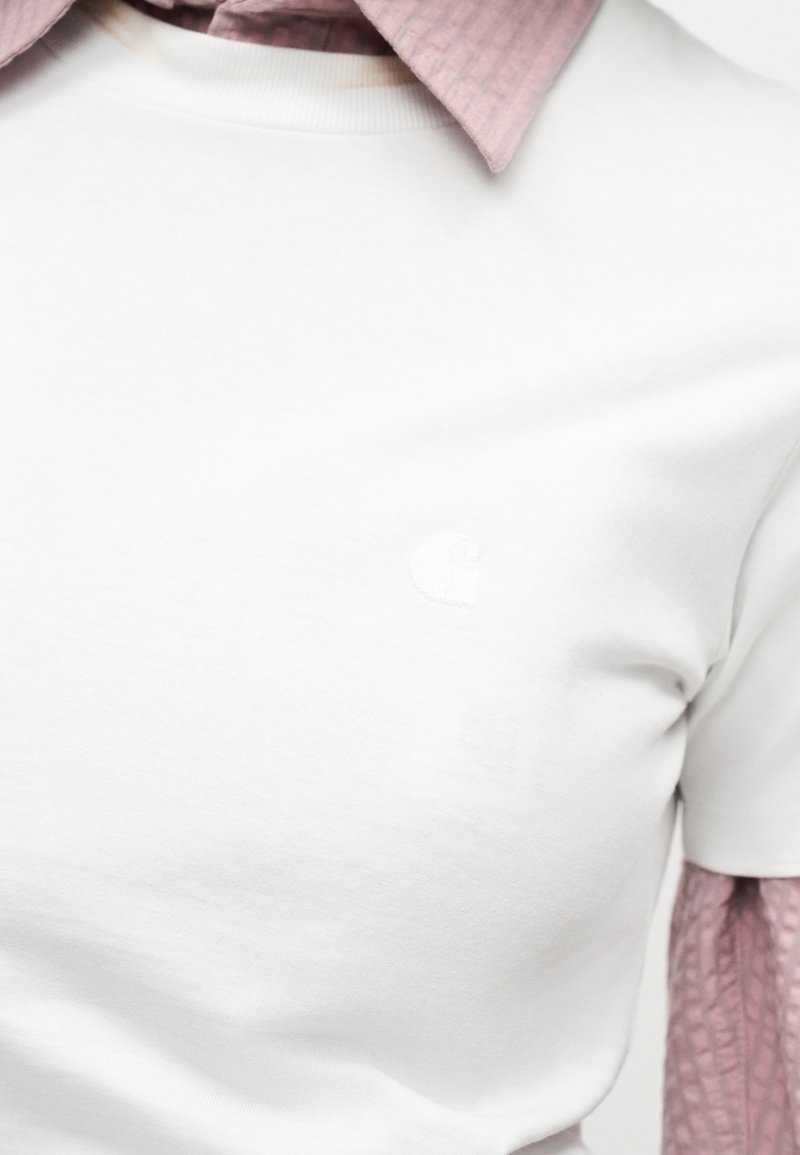 Primo piano di una camicia bianca a maniche corte indossata sopra una camicia a maniche lunghe texturizzata color malva con colletto.