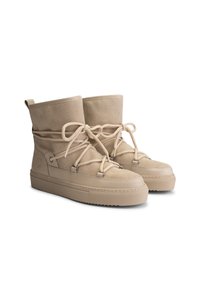 Pair of beige suede winter boots with thick rubber soles and crisscross rope laces tied in bows, positioned side by side.