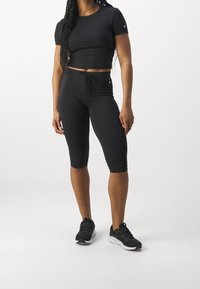 Czarny krótki t-shirt i capri legginsy z wysokim stanem wykonane z elastycznego materiału. Posiadają ściągacz w talii i logo na elementach.