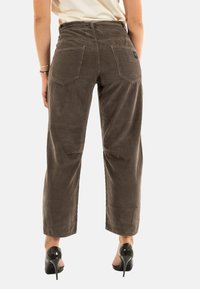 Pantaloni in corduroy marroni con gambe ampie, tasche posteriori e un motivo a coste testurizzato, abbinati a scarpe con tacco nere.