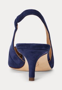 Donkerblauwe suède slingback pump met een middelhoog taps toelopend hakje en een beige zool, gezien van achteren.