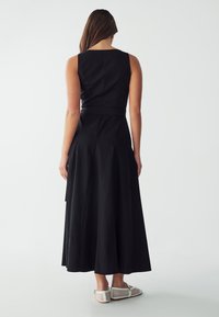 Mustat hihattomat mekko, jossa on tiukka yläosa, levenevä hame ja sivusiteet. Kankaan tekstuuri on mielenkiintoinen. Yhdistetty valkoisten kudottujen slip-on-kenkien kanssa.