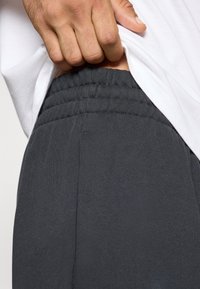 Pantalones deportivos grises con un acabado texturizado y cinturilla elástica, parcialmente cubiertos por una camisa blanca. Detalle visible de la costura lateral.