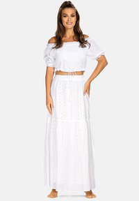 Biała krótka bluzka na ramiączkach z bufkami, z wiązaniem w talii, oraz długa, warstwowa spódnica z wycięciami i zwiewną sylwetką.