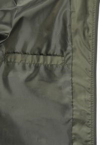 Intérieur de veste en nylon brillant de couleur vert olive avec une seule poche horizontale. Texture lisse et fermeture éclair sur le bord droit.