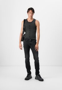 Tricou fără mâneci gri, cu guler rotund, asociat cu blugi strâmți negri și încălțăminte sport neagră. Design minimalist, fără modele.