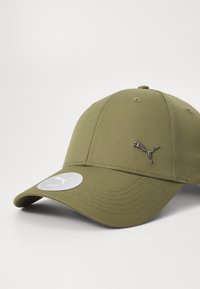 Olive green cap made of textured fabric with a curved brim, featuring a silver embroidered logo and a circular tag on the visor.