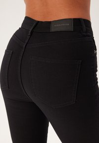 Jeans in denim nero con una vestibilità slim, dotati di vita a media altezza, due tasche posteriori e un'etichetta con la scritta "BUBBLE ROOM" sulla vita.