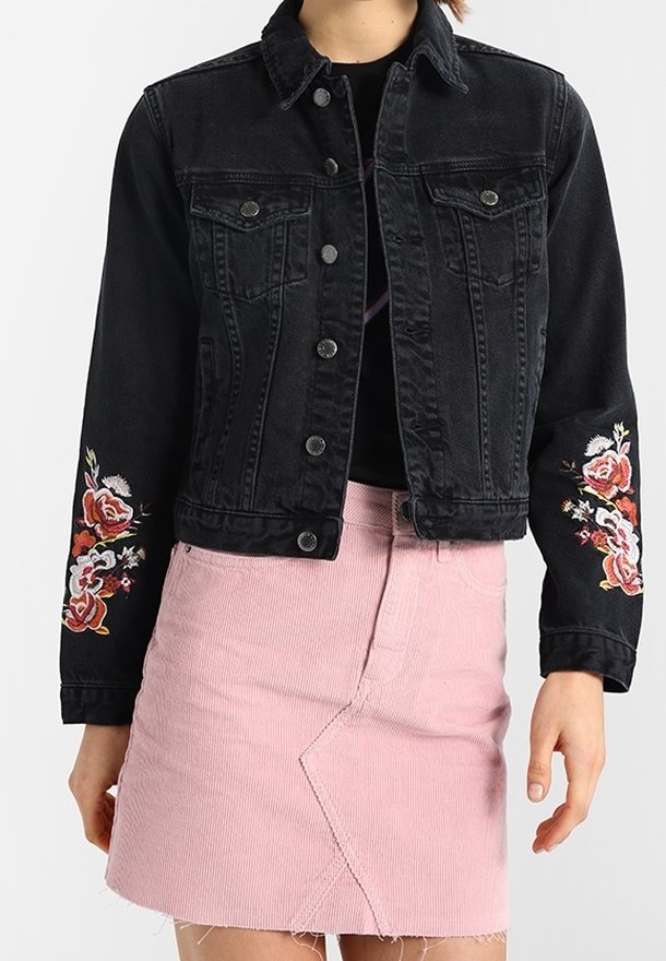 Black denim jacket with embroidered floral designs on sleeves, two chest pockets, and button closure, paired with a light pink corduroy skirt.