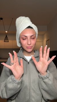 Persona con felpa grigia con cerniera e maniche arricciate, asciugamano bianco avvolto intorno alla testa, con unghie curate che mostrano gesti con le mani.