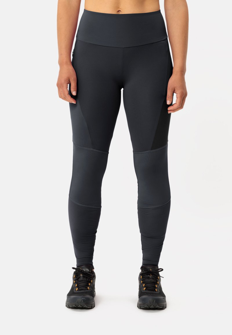 Leggings neri a vita alta con una texture liscia, dotati di pannelli in rete e sezioni di tessuto a contrasto, abbinati a scarpe da ginnastica nere.