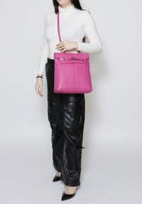 Roze leren handtas met een gestructureerd ontwerp, voorzien van zilverkleurige hardware, een opklapbare klep en een lange verstelbare schouderriem.