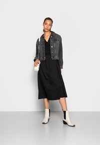 Vestido midi preto com corpete de renda, sobreposto a uma jaqueta de ganga preta desbotada. Botas de tornozelo em creme com painéis laterais pretos e pontas quadradas.