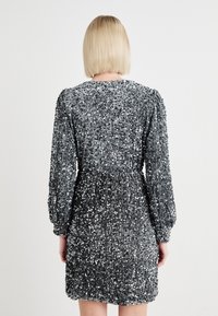 Vestido de mangas curtas, com lantejoulas prateadas, uma cintura ajustada e mangas bufantes, apresentando uma superfície texturizada e decote redondo.