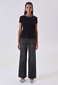 T-shirt nera a maniche corte con scollatura decorativa, abbinata a jeans in denim scuro a vita alta e gamba larga e scarpe argento metallico.