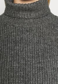 Suéter de cuello alto en gris, hecho de un tejido de punto grueso y acanalado. Textura notable y patrón consistente en todo.