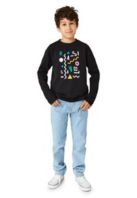 Schwarzes Langarm-T-Shirt mit bunten geometrischen Formen und Text auf der Vorderseite, kombiniert mit hellblauen Jeans und weißen Turnschuhen.