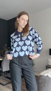 Sveter s jemnými modrými srdcovými vzormi na námorníckom pozadí, s golierom a trojtlakovým zapínaním. Skombinovaný s čiernymi nohavicami.