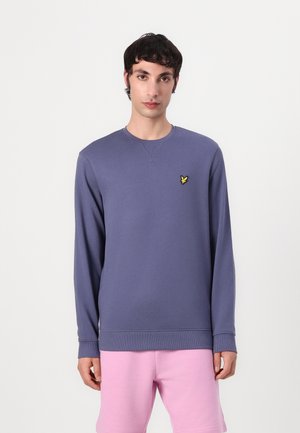 Sweatshirt violet à manches longues, col rond et ourlet côtelé. Présente un petit logo jaune brodé sur la poitrine gauche.