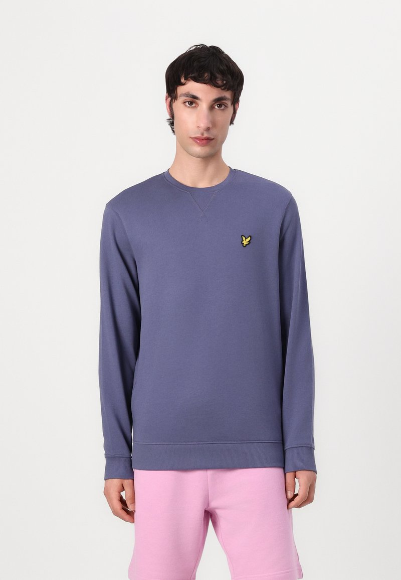 Sweatshirt violet à manches longues, col rond et ourlet côtelé. Présente un petit logo jaune brodé sur la poitrine gauche.