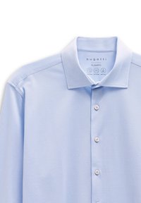 Hellblaues Polohemd aus strukturiertem Stoff mit umgeschlagenem Kragen, sechs Knöpfen auf der Vorderseite und Markentags in der Nähe des Kragens.