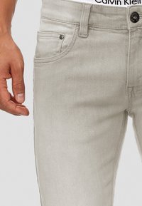 Lichtgrijze denim jeans met een slim fit, voorzien van een voorste muntzakje en een Calvin Klein tailleband. De textuur is soepel met een lichte glans.
